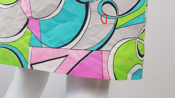 Closeup with Red circled flaws on hem of Vintage 1980s Lady Bayard shirt dress with short sleeves, a pointed collar, button front, matching tie belt, and a bold abstract geometric print in pink, turquoise, lime green, grey, and black displayed on a mannequin