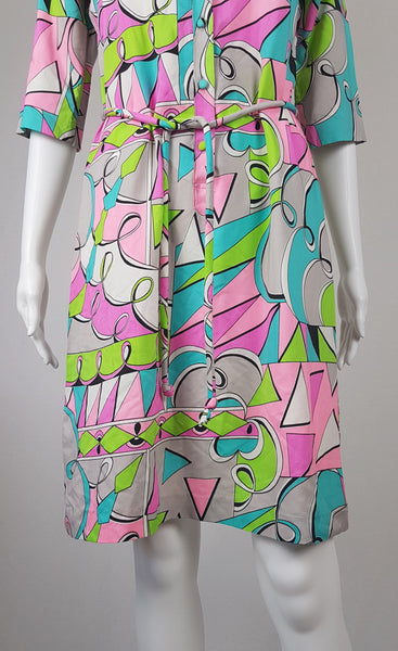 Front view of Vintage 1980s Lady Bayard shirt dress with short sleeves, a pointed collar, button front, matching tie belt, and a bold abstract geometric print in pink, turquoise, lime green, grey, and black displayed on a mannequin