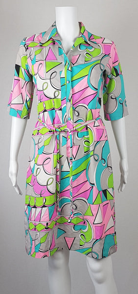 Front view of Vintage 1980s Lady Bayard shirt dress with short sleeves, a pointed collar, button front, matching tie belt, and a bold abstract geometric print in pink, turquoise, lime green, grey, and black displayed on a mannequin