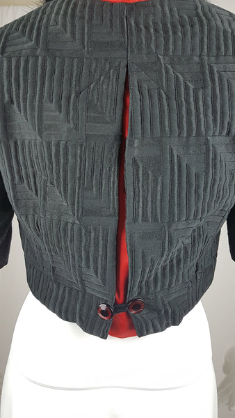 Vintage black brocade cropped bolero jacket with a fur collar, red satin lining, ribbon loop and decorative button displayed on a mannequin - back view