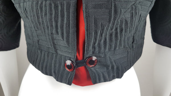 Vintage black brocade cropped bolero jacket with a fur collar, red satin lining, ribbon loop and decorative button displayed on a mannequin - back view