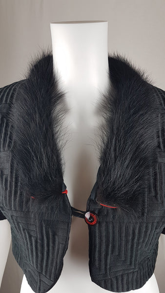 Vintage black brocade cropped bolero jacket with a fur collar, red satin lining, ribbon loop and decorative button displayed on a mannequin - closeup front view