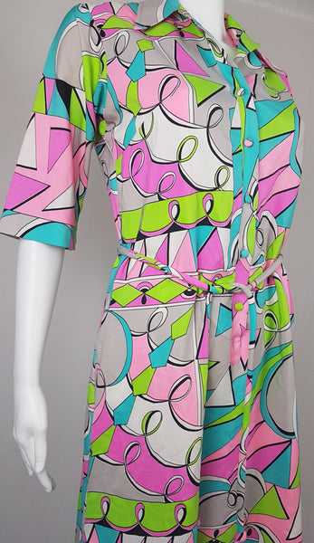 Front view of Vintage 1980s Lady Bayard shirt dress with short sleeves, a pointed collar, button front, matching tie belt, and a bold abstract geometric print in pink, turquoise, lime green, grey, and black displayed on a mannequin
